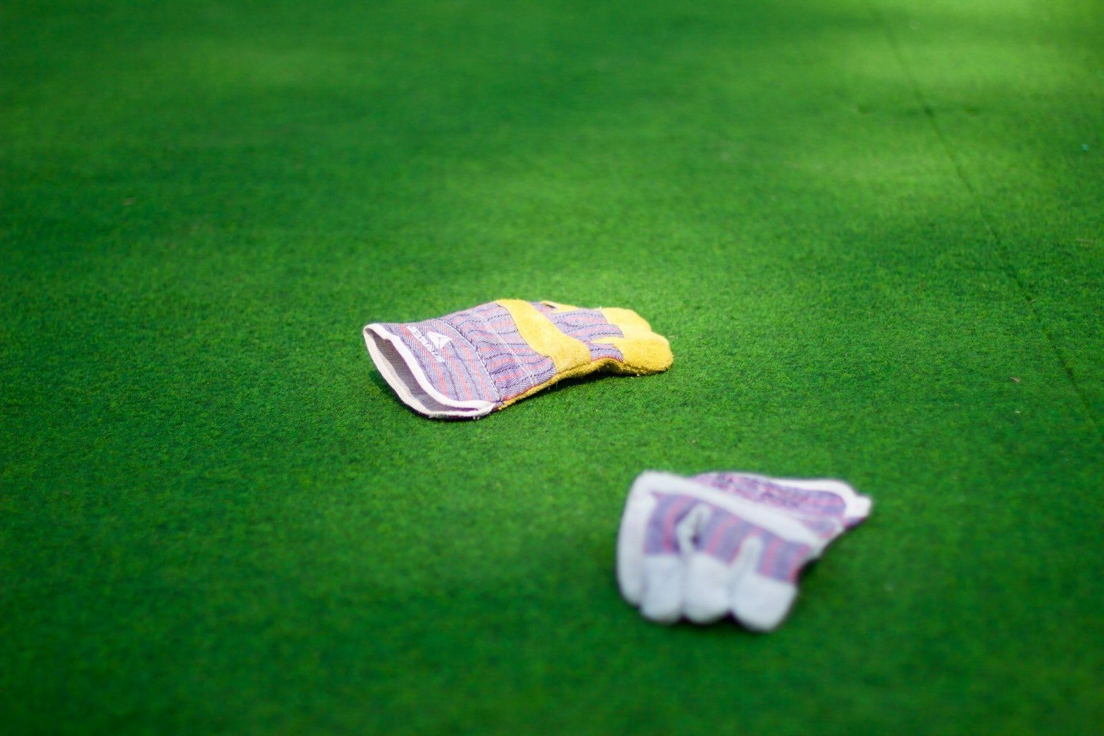 Two colorful gardening gloves are lying on a well-maintained, vibrant green Scottsdale artificial turf. One glove is partially folded over itself, while the other glove is laid out more flatly. The scene is sunlit, highlighting the gloves against the grass, perfect for any sport turf installer Scottsdale AZ could recommend.