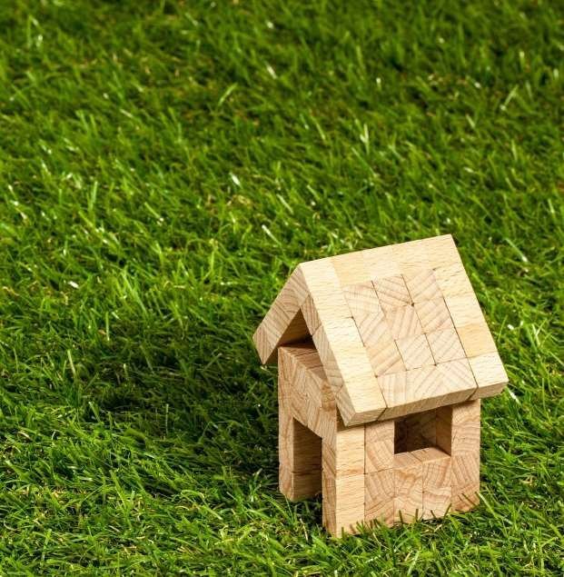 A small wooden block house with a triangular roof sits on lush, green artificial turf, symbolizing simplicity and a natural living environment. For expert pet turf installers in Scottsdale AZ, trust the professionals who prioritize quality and aesthetics.