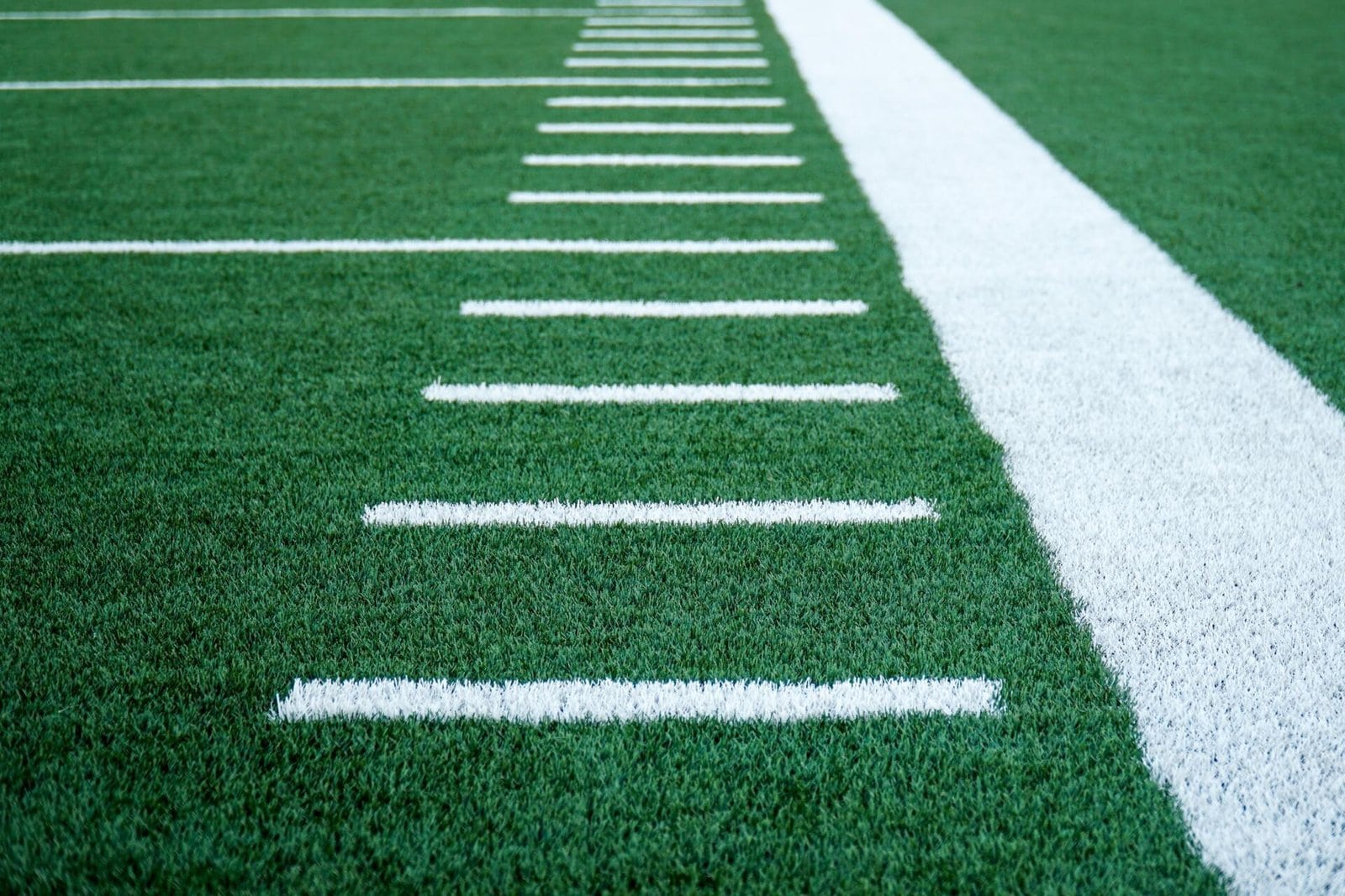 Close-up of a football field in Scottsdale, AZ, showing the yard lines and part of the sideline. The turf, installed by a top rated artificial grass installer, is a deep green with white horizontal lines at regular intervals. A thick white sideline runs vertically through the right side of the image.